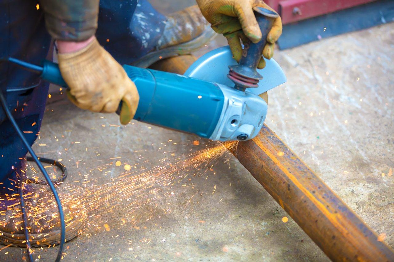 Électricien professionnel utilisant une meuleuse d’angle sans fil pour découper du métal sur chantier.