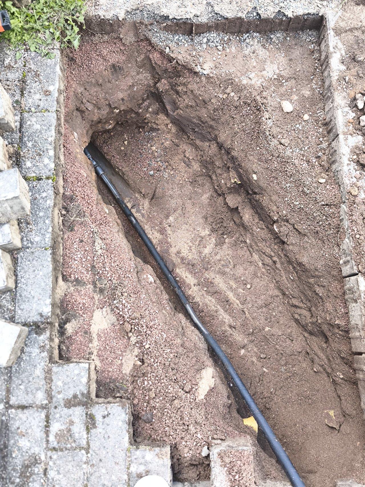 Installation de câbles de jardin dans une tranchée avec grillage avertisseur rouge pour sécurité.
