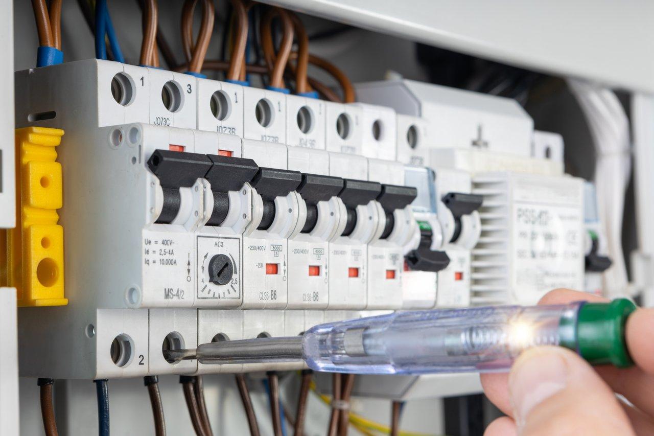 Technicien en inspection électrique utilisant un multimètre calibré pour tester un disjoncteur dans un tableau électrique ouvert.