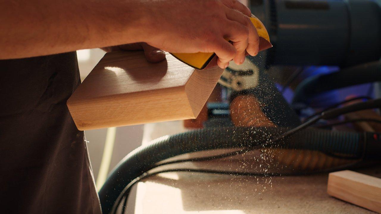 Travailleur sanding wet wood winter, équipé de protections, lors d'un ponçage extérieur humide en hiver.