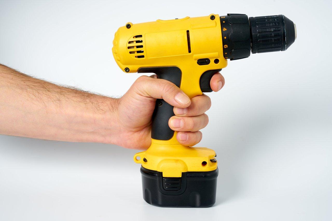 Un électricien professionnel utilisant un drill sans fil jaune et noir pour ses travaux de construction.