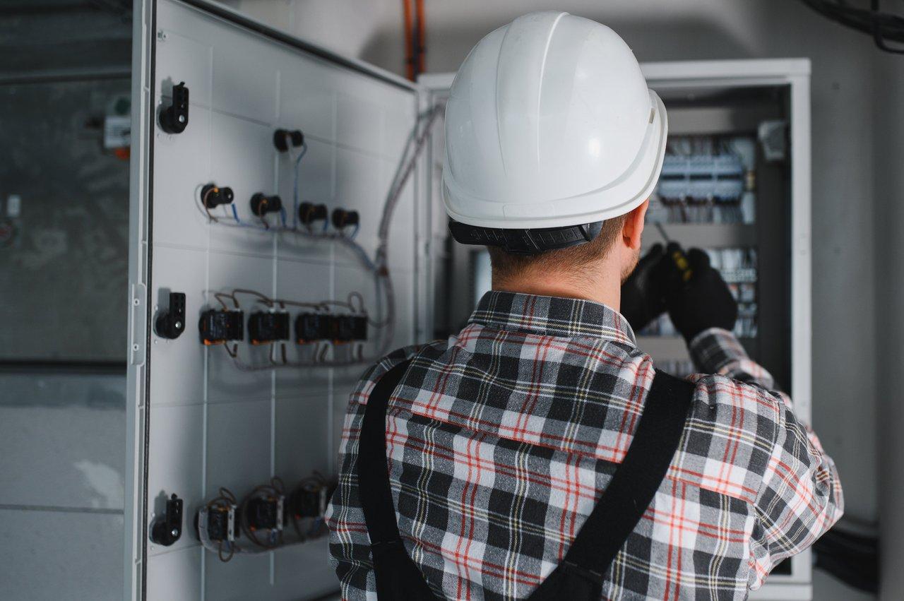 Un technicien certifié réalise une maintenance électrique sécurisée sur un panneau électrique, équipé de protections.