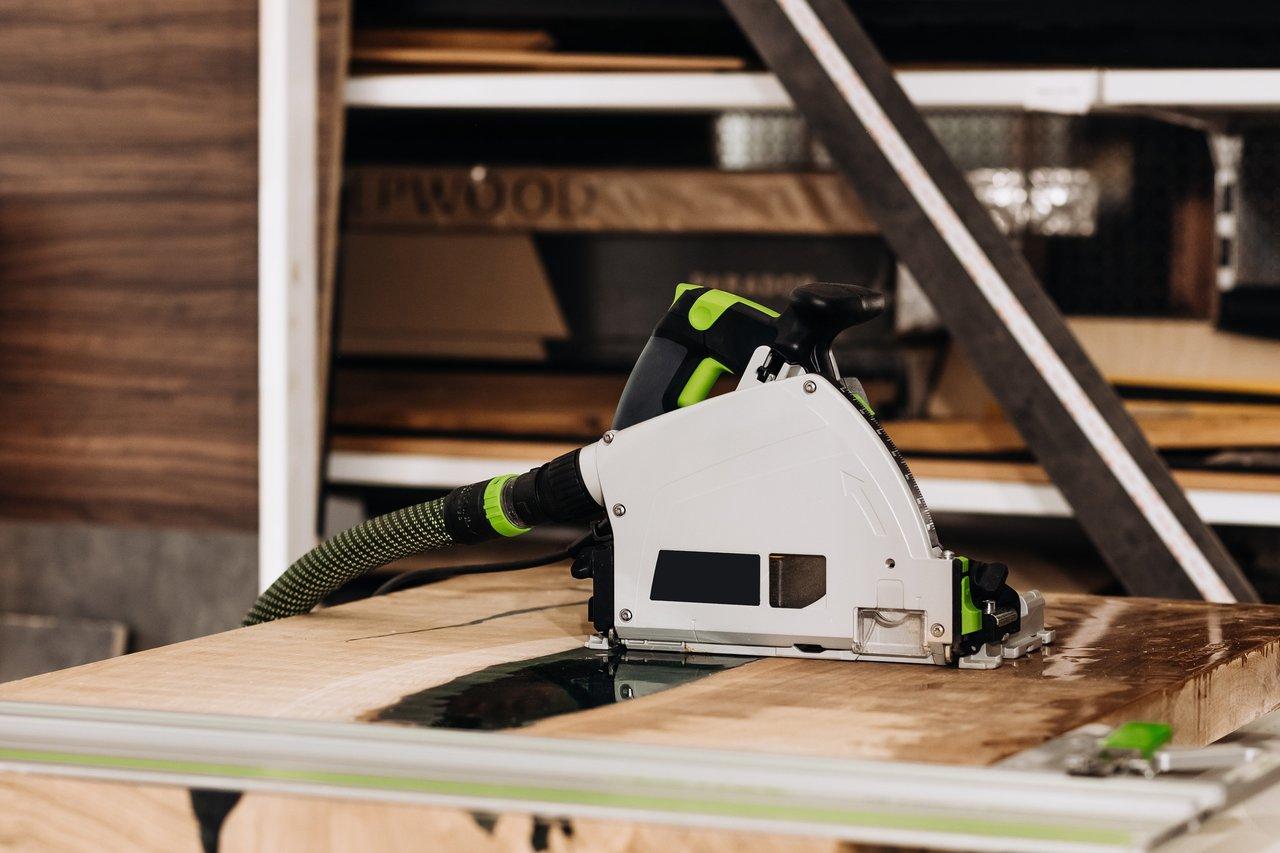 Une scie circulaire plongeante avec rail de guidage et système d’aspiration des poussières en action sur un chantier.